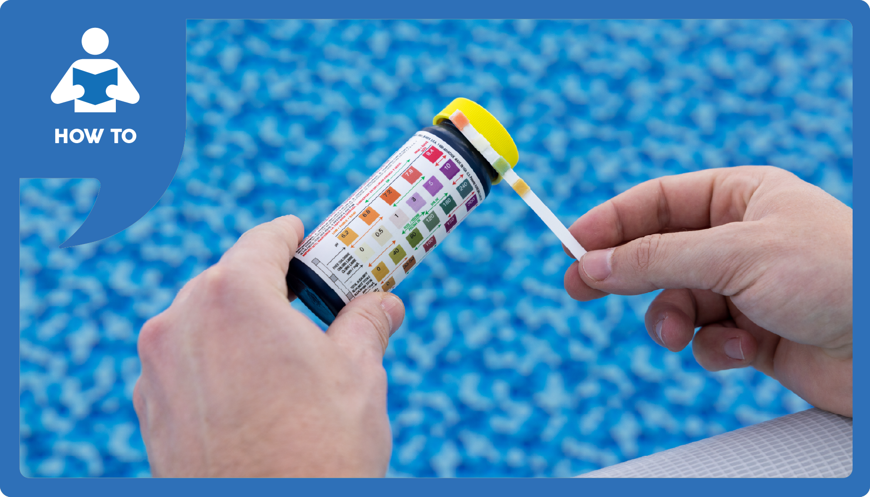 A hand holds a pool test strip next to a color chart over the pool water.