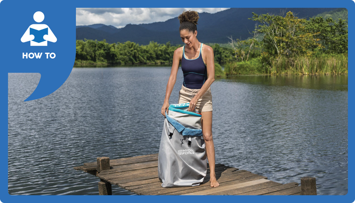 Woman on a dock re-packing her folded SUP into her carry bag with a lake in the background